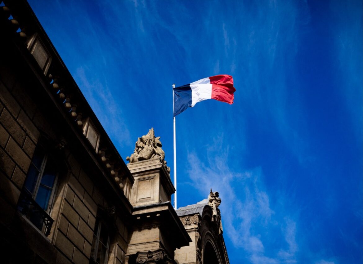French tricolour flag (blue, white and red, symbol of the Republic of France) hanging from a flagpole above the entrance gate to the courtyard of the Elysee Palace, Exit from the Cabinet meeting at the Presidential Palace of the Elysee in Paris, France on August 27, 2025. The ministers get into their cars and leave the Elysee Palace. (Photo by Amaury Cornu / Hans Lucas via AFP)